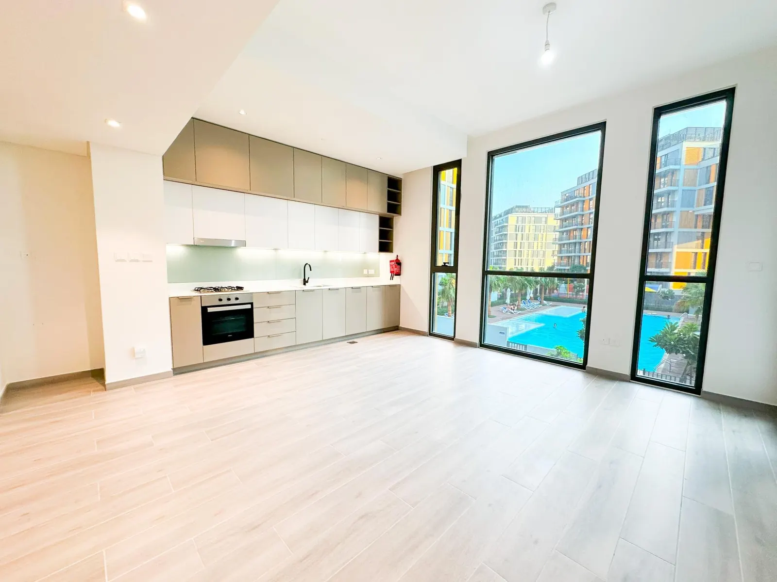 Open kitchen and living room of a one-bedroom apartment in Noor 2, with full-height windows over the pool